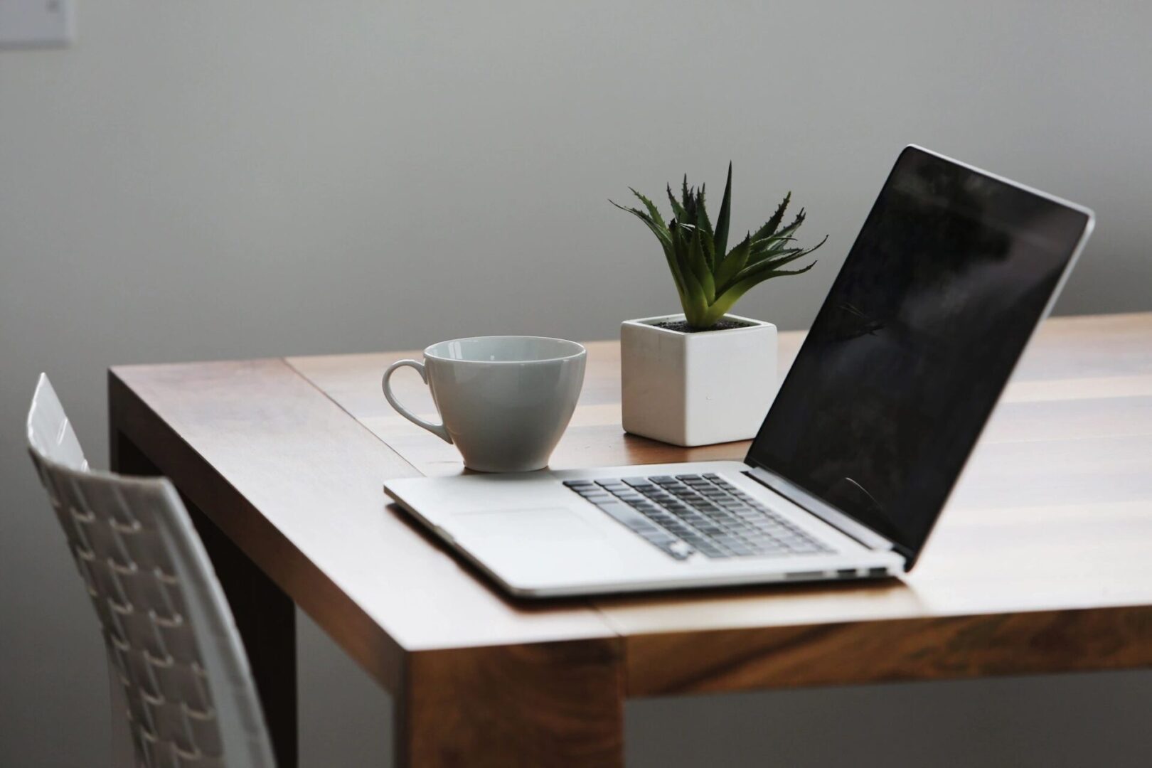 Photo of an open Macbook on a table. There is also a plant and a coffee cup.